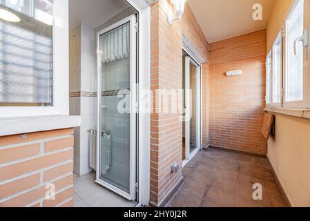 Terrasse fermée dans une maison résidentielle urbaine avec accès à une cuisine carrelée de blanc avec bordure marron Banque D'Images