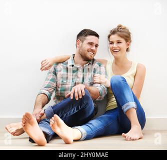 Heureux chaque fois que vous envoyez un message instantané. Photo d'un jeune couple affectueux assis les uns à côté des autres sur le sol à la maison. Banque D'Images