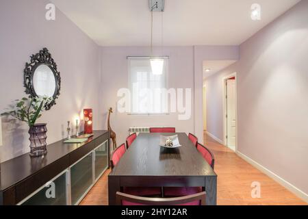 Salle à manger de location de vacances avec meubles en bois sombre avec miroir, décoration, girafe, vase et murs peints au lilas Banque D'Images