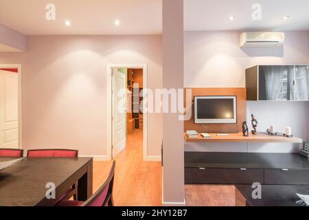 Salle à manger de l'appartement de vacances avec meubles en bois sombre avec miroir, décor, climatisation, tv plasma et tableau de côté et mur peint en lilas Banque D'Images