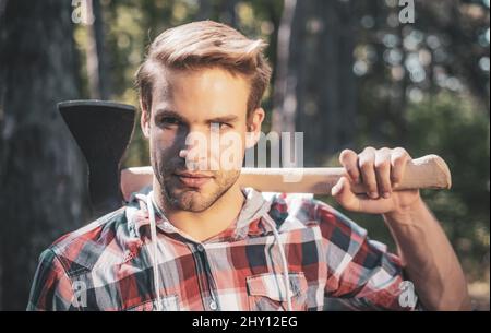 Un beau jeune homme avec une barbe porte un arbre. Beau Woodsworker bûcherons chemise à carreaux tenant la hache sur fond vert nature. Banque D'Images