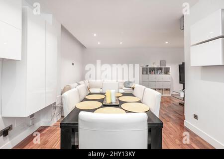 Table à manger noire avec bougies au centre, canapés en cuir d'angle et parquet en acajou, bibliothèque carrée et mobilier en bois blanc clair Banque D'Images