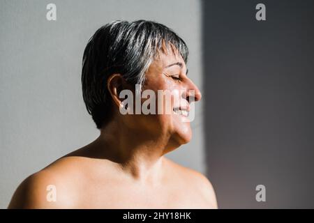 Courte femme non reconnaissable en tricoté chaud gilet orange défilement médias sociaux sur smartphone debout sur un mur de béton Banque D'Images