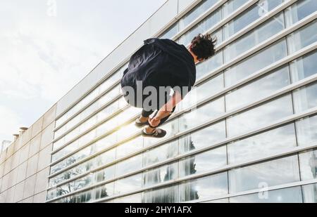 Vue arrière d'un homme anonyme dans des vêtements décontractés sautant et effectuant un tour de parkour dans l'air dans une rue urbaine avec des bâtiments modernes Banque D'Images