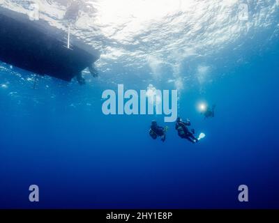Groupe de plongeurs professionnels en combinaisons prenant des photos les uns des autres tout en nageant près de la surface de l'eau avec le bateau sous-marin en haute mer Banque D'Images