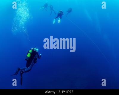 Groupe de plongeurs professionnels en combinaisons prenant des photos les uns des autres tout en nageant près de la surface de l'eau avec le bateau sous-marin en haute mer Banque D'Images