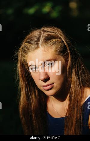 Jeune femme sérieuse avec de longs cheveux ondulés regardant l'appareil photo sur un arrière-plan flou Banque D'Images