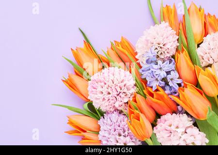 Bouquet de tulipes orange vif et de fleurs de jacinthe roses sur fond lilas. Carte de vœux. Plan à plat, espace de copie pour le texte Banque D'Images