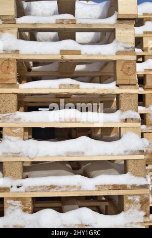 Gros plan de palettes industrielles en bois enneigé empilées les unes sur les autres un jour d'hiver Banque D'Images