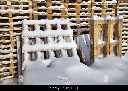 Palettes industrielles en bois enneigé empilées les unes sur les autres les jours d'hiver Banque D'Images