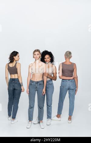 Pleine longueur de femme afro-américaine embrassant un ami blond sur fond gris, image de stock Banque D'Images