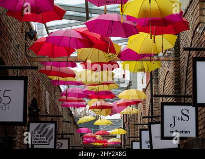 Parasols jaunes et rouges colorés suspendus au-dessus d'une allée pleine de boutiques à Camden Market, dans le nord de Londres. Banque D'Images