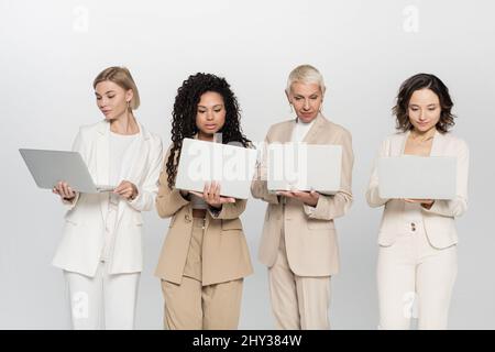 Femmes d'affaires multiethniques utilisant des ordinateurs portables isolés sur gris, concept féminisme, image de stock Banque D'Images