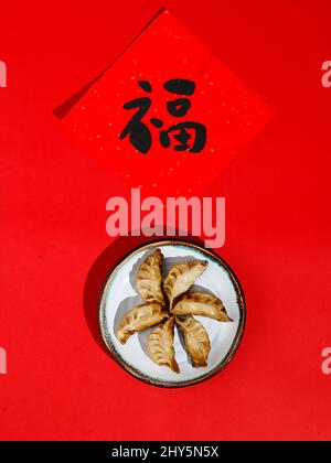 Vue de dessus des boulettes chinoises (Jiaozi) disposées en cercle dans une plaque ronde blanche sur fond rouge Banque D'Images