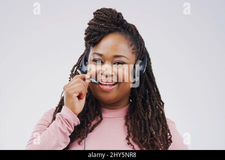 Je suis toujours prêt à aider mes clients. Portrait en studio d'une jeune représentante attirante du service clientèle portant un casque contre un gris Banque D'Images