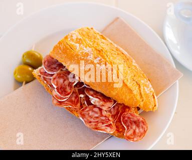 Petit-déjeuner espagnol - sandwich au fuet aux saucisses fumées et olives en gros plan Banque D'Images