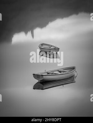 Belle photo en niveaux de gris de deux petits bateaux en bois dans l'eau grise brillante réfléchissante Banque D'Images