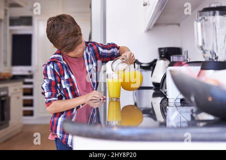 Maman a dit que je pourrais aider myslef. Un jeune garçon boit un verre de jus d'orange. Banque D'Images