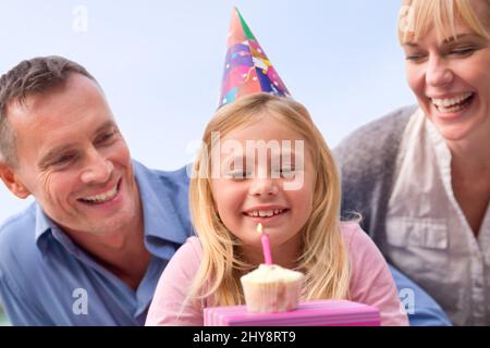 Que dois-je souhaiter ? Une photo courte d'une petite fille heureuse et de ses parents célébrant son anniversaire. Banque D'Images