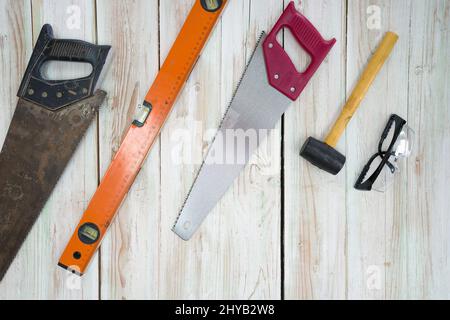 L'équipement de travail du bois est soigneusement organisé sur le plancher en bois. Commandé comme suit, ancienne scie pleine de rouille, niveau d'aluminium magnétique orange, rouge han Banque D'Images