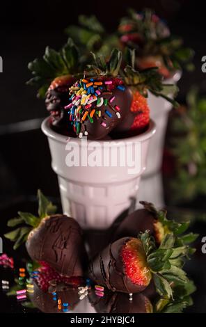 Une dose verticale de fraises enrobées de chocolat et de saupoudriers dans des tasses en verre blanc Banque D'Images