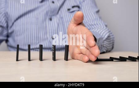 Arrêt de l'effet Domino. Un homme d'affaires ferme la main pour protéger les morceaux de domino contre la chute. Intervention réussie dans les performances de l'entreprise. Photo de haute qualité Banque D'Images