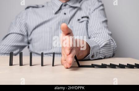 Concept d'assurance. Un homme d'affaires ferme la main pour protéger les morceaux de domino contre la chute. Prévention des crises économiques et des défaillances des entreprises. Photo de haute qualité Banque D'Images