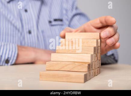 Homme d'affaires à la main empilant des blocs de bois dans l'échelle de carrière. Développement professionnel, croissance, promotion, réalisation des objectifs. Aspiration. Photo de haute qualité Banque D'Images