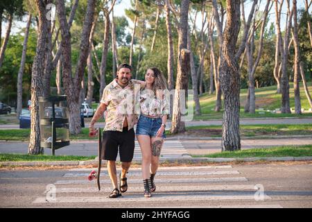 Jeune couple tatoué frais marchant avec une longue planche. Banque D'Images