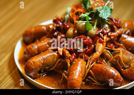 Gros plan du plat traditionnel de écrevisses chinoises épicées dans une assiette blanche sur une table en bois Banque D'Images