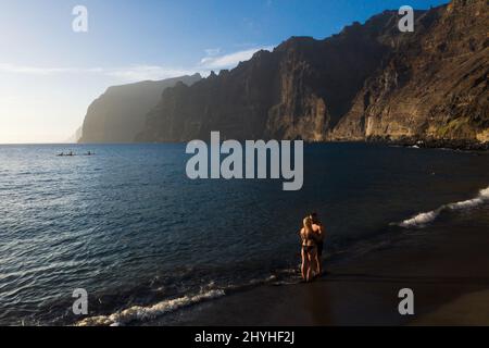 Un couple amoureux se tient sur une plage noire près des rochers d'Acantilados de Los Gigantes au coucher du soleil, Ténérife, îles Canaries, Espagne. Banque D'Images