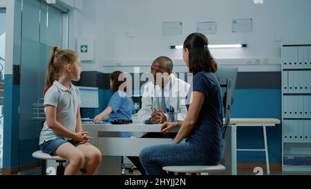 Médecin saluant la petite fille et la mère dans le cabinet médical. Médecin et patient de sexe masculin ayant une conversation sur la maladie et le traitement sur ordonnance lors de la visite de contrôle annuelle. Service de santé Banque D'Images