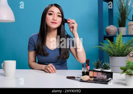 Vlogger asiatique faire le tutoriel de maquillage en utilisant le pinceau à l'appareil photo enregistrement podcast pour le canal de vlogging en studio. Un influenceur de médias sociaux filmant un produit publicitaire de contenu de cosmétiques de beauté Banque D'Images