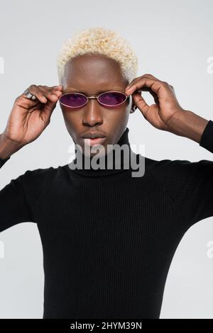 homme afro-américain blond à col roulé portant des lunettes de soleil roses isolées sur le gris Banque D'Images