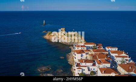 Tir de drone, vieille ville de Chora, maisons aux toits de tuiles rouges, forteresse en ruines sur l'île offshore, phare rond blanc sur le rocher, bateau se déplaçant de gauche Banque D'Images