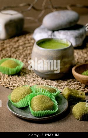 Dessert de riz asiatique traditionnel mochi de matcha vert doux avec une tasse de thé matcha mousseux et de poudre de matcha verte dans une assiette en céramique sur une table brune. Natura Banque D'Images