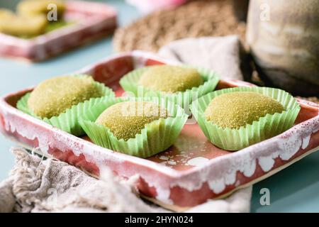 Gros plan du dessert de riz traditionnel asiatique mochi de matcha vert doux dans un plat de céramique rose sur une table bleue. Banque D'Images