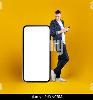 Homme près du grand téléphone portable debout en utilisant le téléphone sur fond jaune Banque D'Images