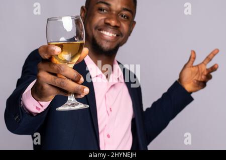 Un jeune homme noir enthousiaste élève un verre de vin sur un fond violet clair Banque D'Images
