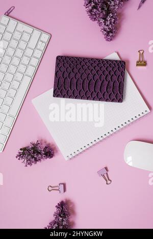 Clavier et souris, carnets, stylo, bouquet de lilas sur fond rose. Fleurs de printemps pourpres. Composition pour un blogueur Banque D'Images