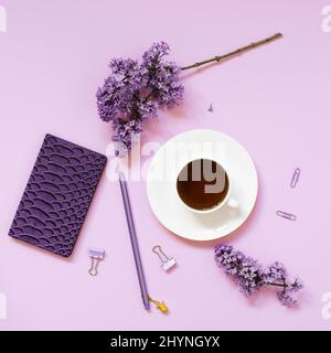 Une tasse de thé, des carnets, un stylo, un bouquet de lilas sur fond violet. Fleurs de printemps pourpres. Pause thé au travail blogueur ou employé de bureau Banque D'Images