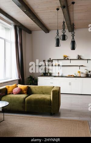 Canapé en velours vert avec oreillers lumineux dans le salon scandinave avec cuisine Banque D'Images