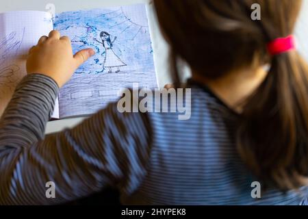 Une petite fille peint une image avec des crayons. Photo prise à la lumière du jour depuis la fenêtre. Banque D'Images