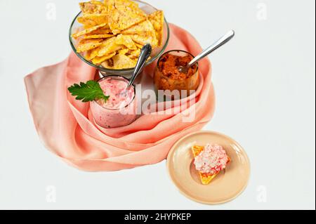 Deux tartiner (tomate et poivron rouge, saumon), petite assiette avec papillote, papillote de maïs dans un bol en verre emmêlé dans une écharpe rose sur fond blanc. Banque D'Images