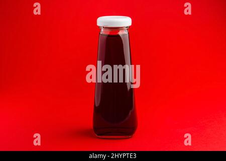 Bouteille avec boisson liquide rouge haltée sur fond de poivre rouge. Jus de cerise Banque D'Images