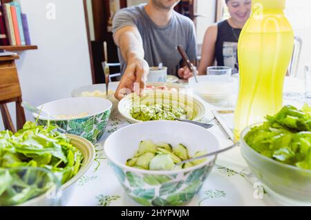 jeune homme caucasien assis à côté de sa petite amie mangeant en prenant avec sa main un bol avec guacamole de la table Banque D'Images