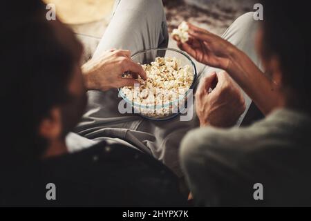 Je suis vraiment ravi de partager du pop-corn. Photo d'un jeune couple assis sur un canapé et sur du pop-corn à la maison. Banque D'Images