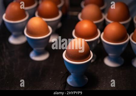 Gros plan sur les œufs de poulet marrons bouillis dans un coquetier blanc sur plateau noir, mise au point, lumière et ombre sélectionnées. Banque D'Images