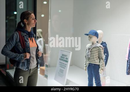 Une jeune femme se tient près de la fenêtre du magasin de vêtements pour enfants Banque D'Images