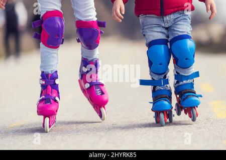 Enfants garçon et fille s'amuser à l'extérieur tout en faisant des patins à roulettes. Enfants sur les rollers. Patinage à roulettes dans le parc près de la mer. Banque D'Images